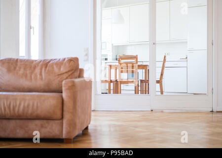 Apartment mit einem Wohnzimmer mit Holzfußboden, einer Couch und einer Küche im Hintergrund Stockfoto