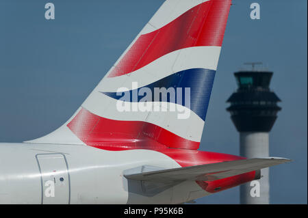 Die heckflosse eines British Airways Airbus A 319-131 entlang der Start- und Landebahn vor dem Kontrollturm am Flughafen Manchester rollen. Stockfoto