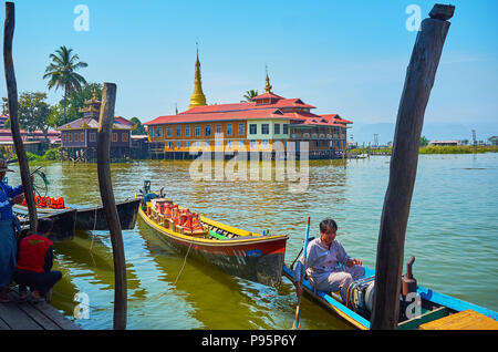 YWAMA, MYANMAR - 18. Februar 2018: Der Blick auf das buddhistische Kloster durch die alten hölzernen Pfosten für das Festmachen von Kajaks im Hafen auf dem Inle See, auf F Stockfoto