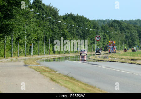 This road looks wet, but it is not, it is a mirage caused by a layer of hot air over the asphalt, heat distortion also obscuress the structures most f Stockfoto