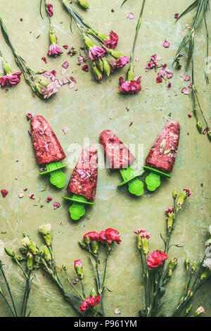 Red hausgemachte Obst und Beeren Eis oder Eis am Stiel auf Teal rustikalen grünen Tisch Hintergrund, mit Garten Blumen, Ansicht von oben eingerichtet. Country Style Stockfoto