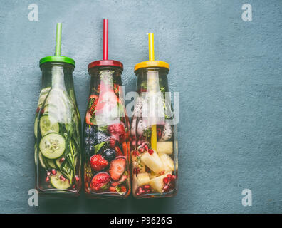 Vielfalt von bunten infundiert Wasser in Flaschen mit Früchten, Beeren, Gurken, Kräuter und trinken Strohhalme auf grauem Hintergrund, Ansicht von oben. Lecker Sommer sauber sein Stockfoto