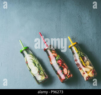 Bunte infundiert Wasser in Flaschen mit Früchten, Beeren, Gurken, Kräuter und trinken Strohhalme auf grauem Hintergrund, Ansicht von oben. Leckere Getränke für den Sommer reinigen Stockfoto