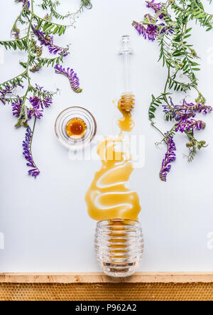 Honey Comb und Pendelarm mit Honig Flecken aus Glas mit wilden Blumen auf weißem Hintergrund, Ansicht von oben Stockfoto