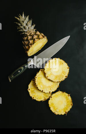 Reife Ananas in Scheiben geschnitten auf konkrete schwarz Tabelle countertop einfachen Hintergrund. Gesunde Ernährung Essen Konzept. Stockfoto