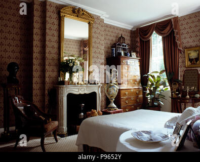 Antiker Spiegel über dem Kamin in 90er Schlafzimmer mit braunen Tapeten und gerafften Vorhängen und angebundene Stockfoto