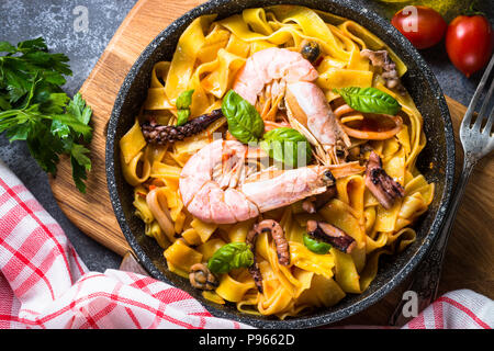 Nudeln mit Meeresfrüchten. Nudeln mit Tintenfisch, Garnelen, Tintenfisch und Muscheln in Tomatensoße. Draufsicht auf schwarz Tisch aus Stein. Stockfoto