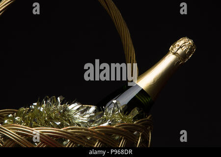 Eine grüne Flasche Champagner in einem Strohkorb mit auf das Neue Jahr Lametta und Früchte auf schwarzem Hintergrund Stockfoto