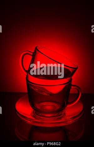 Zwei Glas transparent Tasse mit Tee und Untertasse auf einer rot-schwarzen Hintergrund Stockfoto
