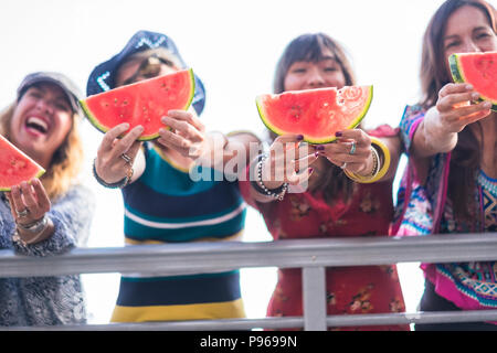 Vier schöne glückliche junge Frauen kaukasischen Essen Wassermelone Sommer und warmen Tag mit Sonne in der Nähe des Ozeans zu feiern. schöne Farben für die Gruppe Stockfoto