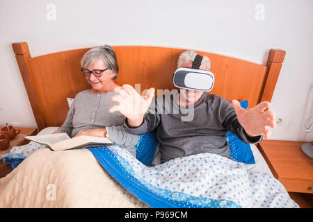 Schön schönes Paar kaukasischen reift der Mann und die Frau zu Hause im Schlafzimmer auf dem Bett während eines Morgen. Sie ein Buch aus Papier lesen und er spielen und u Stockfoto