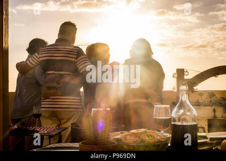 Menschen Gruppe von älteren Freunden Umarmung und zusammen großartig Anzeigen der golde Sonnenuntergang von der Dachterrasse. Wohnen immer in Urlaub und Ruhestand happi Stockfoto