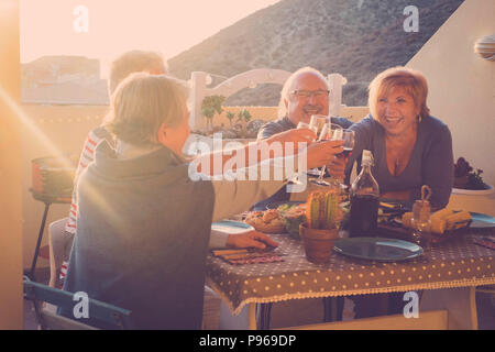 Glückliche Gruppe der Erwachsenen feiern eine Veranstaltung mit Cups von Wein im Freien auf der Terrasse mit Sonnenuntergang und Hintergrundbeleuchtung. goldenen Tönen für Glück lifestyle Conc Stockfoto