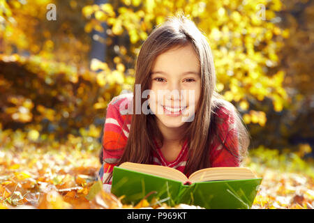 Mädchen liegt auf Laub und ein Buch lesen Stockfoto
