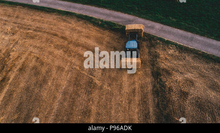 Luftaufnahme der Ernte Feld mit Traktor bewegt sich Hay um von Oben nach Unten Stockfoto