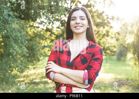 Lächelnd schöne Brünette Mädchen in einem roten, Plaid Shirt, mit verschränkten Armen Stockfoto