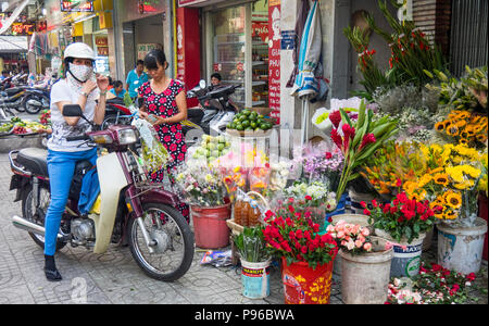 Eine weibliche Motorradfahrer auf Ihrem Motorrad kaufen Blumen vom Floristen auf dem Bürgersteig in Ho Chi Minh City, Vietnam. Stockfoto