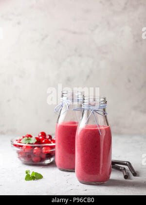 Smoothies cranberry in Flaschen, frische Cranberries in einer Schüssel auf einem grauen konkreten Hintergrund Stockfoto