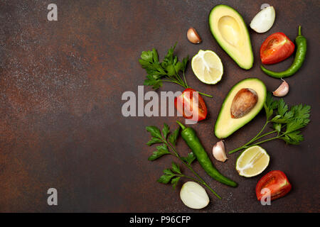 Zutaten für Guacamole: Avocado, Kalk, Tomaten, Zwiebeln und Gewürze auf einem braunen Hintergrund. Blick von oben. Kopieren Sie Platz Stockfoto