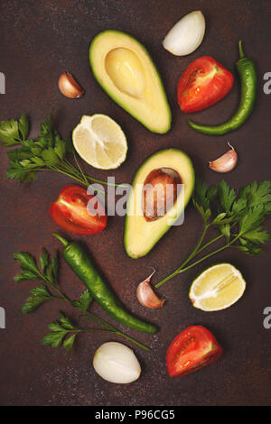 Zutaten für Guacamole: Avocado, Kalk, Tomaten, Zwiebeln und Gewürze auf einem braunen Hintergrund. Blick von oben. Stockfoto