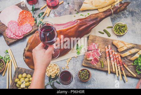 Mans hand Wein Glas frome über Relationen mit spanit oder italienische Vorspeisen, ganzes Bein der Schinken Serrano und Rot einer Rose Wein Stockfoto