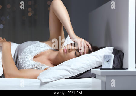 Frau mit Kopfschmerzen mit der Hand auf die Stirn auf dem Bett zu Hause liegen in der Nacht Stockfoto