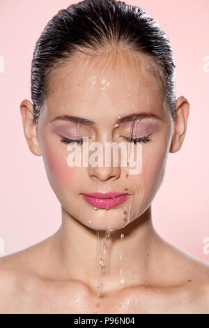 Schönes Modell Mädchen mit Spritzwasser im Gesicht. Schöne Frau unter Wasser mit frischen Haut über rosa Hintergrund. Hautpflege Reinigung und feuchtigkeitsspendende Konzept. Schönheit Gesicht Stockfoto