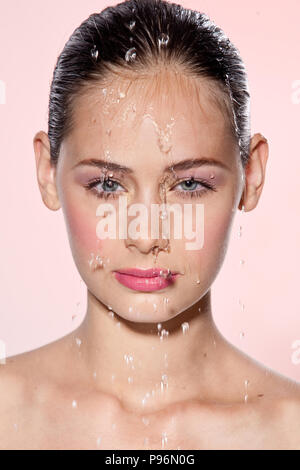 Schönes Modell Mädchen mit Spritzwasser im Gesicht. Schöne Frau unter Wasser mit frischen Haut über rosa Hintergrund. Hautpflege Reinigung und feuchtigkeitsspendende Konzept. Schönheit Gesicht Stockfoto