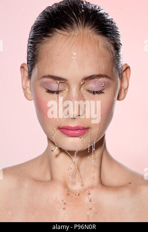 Schönes Modell Mädchen mit Spritzwasser im Gesicht. Schöne Frau unter Wasser mit frischen Haut über rosa Hintergrund. Hautpflege Reinigung und feuchtigkeitsspendende Konzept. Schönheit Gesicht Stockfoto