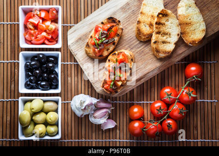 Bruschetta tomate Basilikum und Oliven, Komposition mit Holz Schneidebrett Ansicht von oben. Stockfoto