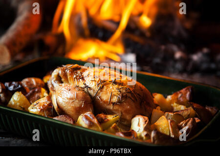 Ein ganzes Hähnchen in Pfanne mit Kartoffeln und ein Kamin im Hintergrund. Stockfoto