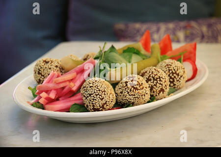 Falafelkugeln in Sesam in einer Schüssel zusammen mit der traditionellen begleitenden Gemüse abgedeckt. Stockfoto