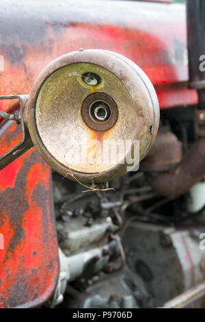 Die gebrochenen Scheinwerfer auf einem alten verrosteten roten Traktor von Massey Ferguson Stockfoto