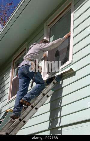 Ein Mann auf einem metallischen Leiter, Austausch der Fenster in der zweiten Etage eines Hauses ausgeglichen an einem sonnigen Herbsttag Stockfoto