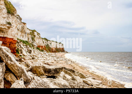 Bewölkten Tag Scrambling entlang der markanten Kreide und Sand Felsen in Hunstanton (North Norfolk, UK) mit der relativ ruhigen Meer Läppen am Strand. Stockfoto