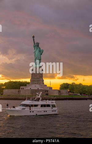 Sonnenuntergang Blick auf die Freiheitsstatue mit Segelboot vorbei in den Hafen von New York Stockfoto