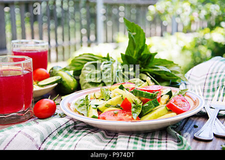 Frühstück im Garten. Salat von Tomaten und Gurken mit grünen Zwiebeln und Basilikum. Stockfoto