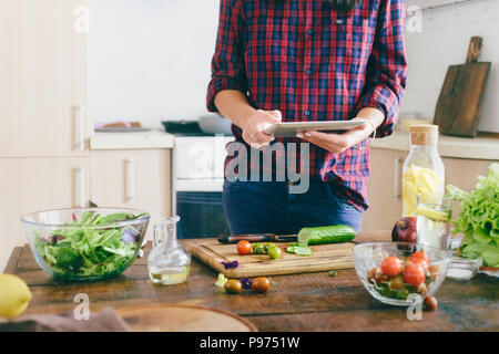 Junge Frau auf der Suche nach einem Rezept für gesundes Essen in der Tablette zu Hause in der Küche. Gesunde Ernährung Konzept Stockfoto