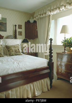 Bett aus Holz mit gedrechselten Spindeln in kleinen Schlafzimmer mit cremefarbenen Vorhängen Stockfoto