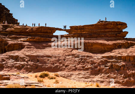 Touristen für Foto steht auf riesigen natürlichen Arch Rock Bridge Posing, Wadi Rum wüste Tal, Jordanien, Naher Osten