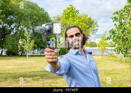 Kerl mit dem Telefon auf dem Stabilisator, nimmt er sich selbst zur Kamera Smartphone Kamera Stockfoto