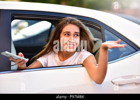 Schöne Frau mit Telefon lächeln beim Sitzen auf dem Rücksitz im Auto. Stockfoto