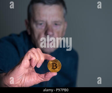 Älterer Mann hält eine bitcoin auf Armlänge Stockfoto