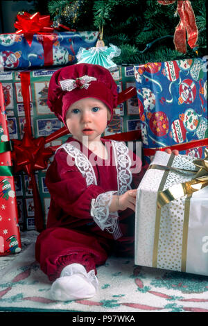 Ein Jahr alten Baby Mädchen sitzen unter Weihnachtsbaum mit Geschenken HERR © Myrleen Pearson Ferguson Cate Stockfoto