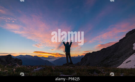 Mann, der auf dem Berg oben Anheben der Arme, sunrise licht bunt Sky scenis Landschaft, die Eroberung des Erfolg LEADER-Konzept. Stockfoto