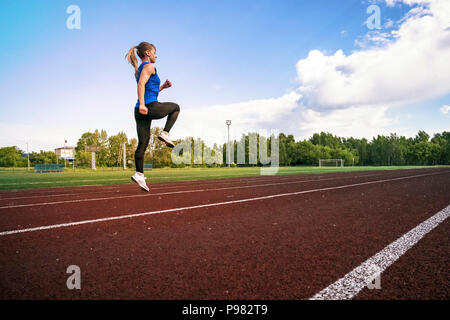 Seitenansicht eines passen junge blonde Frau, Jogging im Stadion. Ein junger Athlet läuft in Sportswear im Stadion in den frühen Morgen. Stockfoto