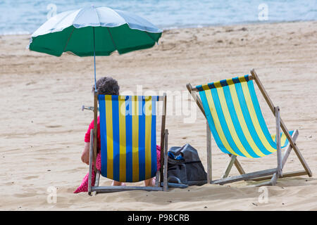 Bournemouth, Dorset, Großbritannien. Juli 2018. Wetter in Großbritannien: Sonnenschein in Bournemouth, aber mit zunehmender Wolkendecke, wenn Sonnenanbeter an die Küste von Bournemouth fahren, um das schöne Wetter zu genießen, bevor es bricht. Frau in Liegestuhl mit Sonnenschirm am Bournemouth Strand, Liegestühle. Quelle: Carolyn Jenkins/Alamy Live News Stockfoto