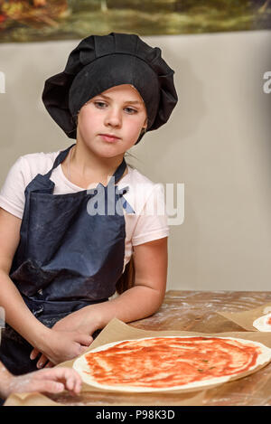 Kleine Mädchen in Uniform bereitet Pizza Kochen in der Küche. Stockfoto