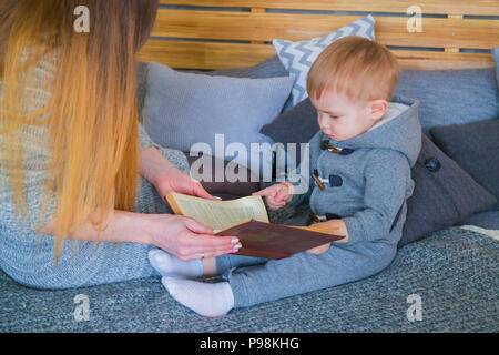 Die junge Mutter und ihr Baby Sohn auf dem Bett zu sitzen und lesen Boo Stockfoto