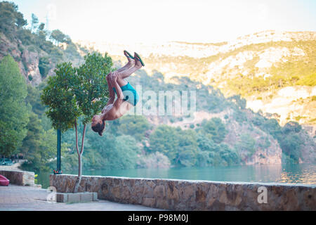 Junger Mann eine Seite blättern oder Salto beim Üben Parkour auf einem See in die Landschaft. Stockfoto